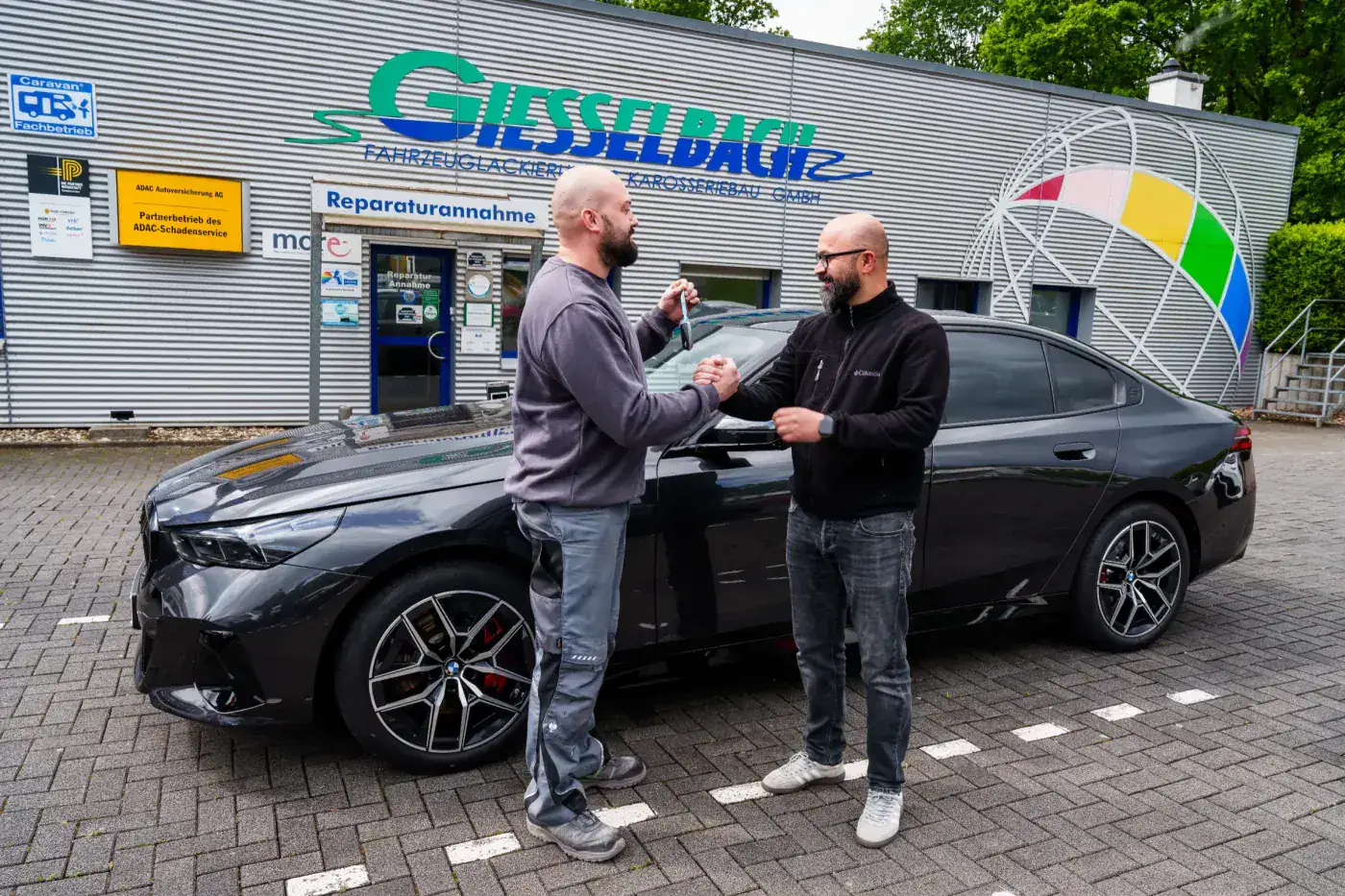 Schlüsselübergabe des wiederaufgebauten Fahrzeugs vor der Werkstatt Giesselbach